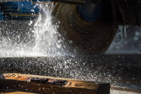 Water sprays into the air as a wheel spins over wooden planks during processing in a sunlit workshop, creating a lively scene