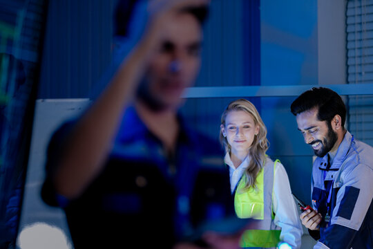 A construction engineer uses a tablet to review a BIM (Building Information Modeling) file. A CAD blueprint of a residential smart building is on a screen in the control center.