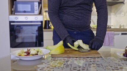 Prepare a delicious and healthy fruit salad in a modern kitchen. A person wearing black gloves carefully cuts fresh melon and adds it to a vibrant fruit mix, emphasizing healthy eating.