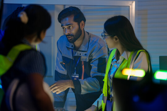 An Indian supervisor leads a night shift briefing in a smart factory control room. He discusses an AI automation system or incident response with his female engineers. - Powered by Adobe