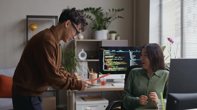 Medium long shot of two young Asian colleagues exchanging lucky red envelopes while celebrating Tet in modern office