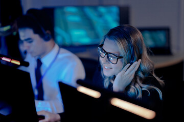 Dynamic night shift collaboration. Male manager provides guidance to a focused male colleague wearing a headset at his computer in a modern tech office during an intense work session.