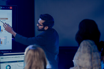 Professional data analysts team collaborating on digital strategy at night. Diverse group examining complex business charts and futuristic dashboard screens in a modern high-tech office environment.