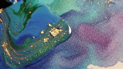 Artistic background of watercolor painting process featuring brushwork, close ups of shimmering gold flakes and liquid blue hues, and scissors resting beside a finished artwork.