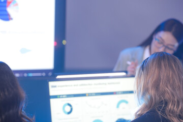Rear view of female analysts monitoring global data maps and business charts on high-tech dashboard screens. Team tracking international statistics in a modern digital command center.