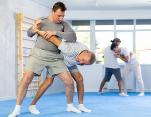 Adult man and elderly men training judo techniques in studio..