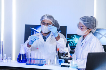 Diverse team of scientists in protective gear collaborating in modern blue lab, analyzing DNA helix structure on monitor and testing chemical samples for medical research.