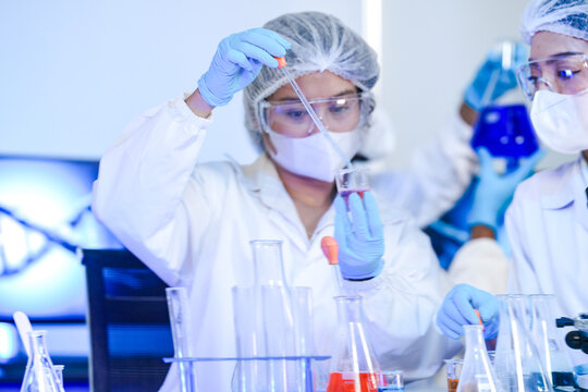 Two focused South Asian scientists, man and woman in lab coats and blue gloves, collaborating to examine a red biological sample slide in a modern research laboratory for medical diagnosis.