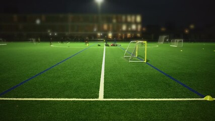 Night view of a football training session on an artificial turf field under bright floodlights with small goals and cones set up for youth practice. - Powered by Adobe