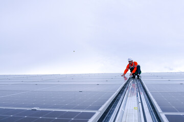 Male technician in safety helmet installing solar panels on factory rooftop, inspecting connections...