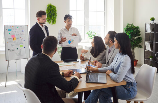 Focused businesswoman steers work meeting for coworkers in office, guiding conversation, anchoring a community of partnership with business people engage deeply in professional interaction.