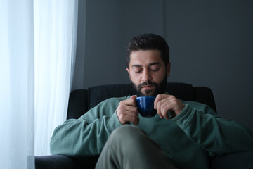 Man relaxing with a warm drink while sitting near a window.