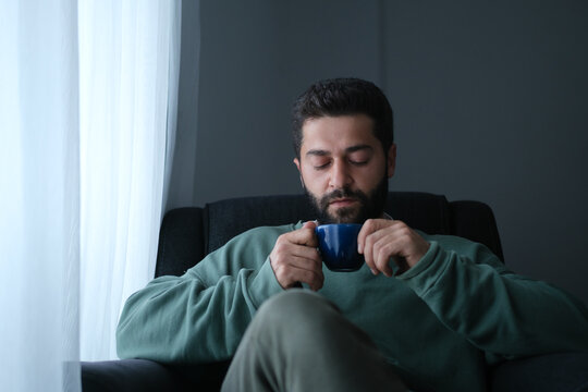 Man relaxing with a warm drink while sitting near a window.
