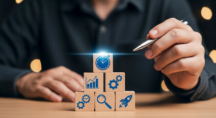 A person s hand holding a pen points to a glowing cube with a clock icon atop a pyramid of wooden blocks featuring business and technology icons symbolizing strategy and innovation