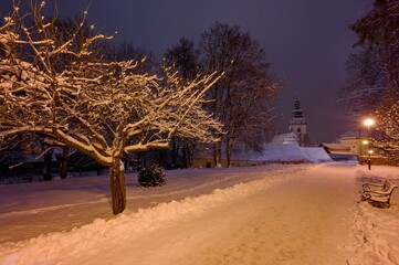 View of the path through the Dean's Garden in Pelhřimov 2025, in the background the tower of the Church of St. Bartholomew, street lighting, clean snow cover,