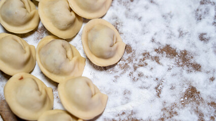 A plate of dumplings is placed on a wooden table with a white powdery substance on the table. The dumplings are arranged in a neat row, with some of them slightly overlapping each other