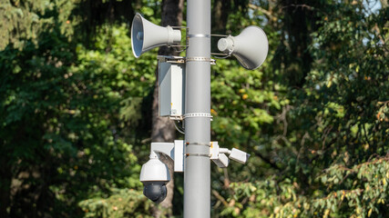 A pole with a camera and a microphone on top. The pole is surrounded by trees