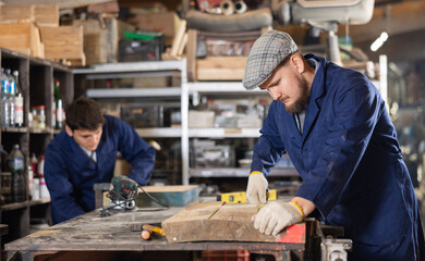 Young man worker measures wooden plank with tape measure in wood workshop
