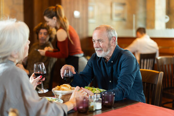 Happy senior couple enjoying relaxed dinner together in cozy restaurant while talking and sharing wine
