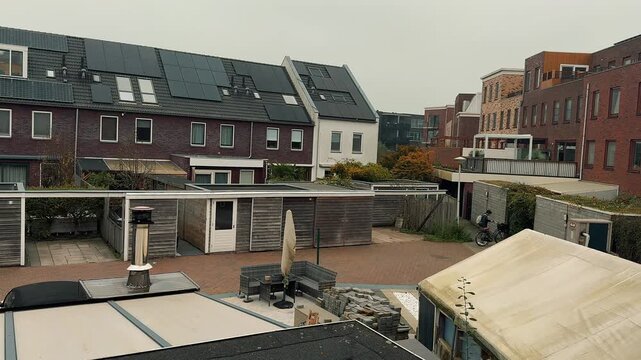 Quiet residential street with brick row houses and solar panels, followed by a view of a red bicycle path in a modern Dutch neighborhood during a cloudy autumn day.

