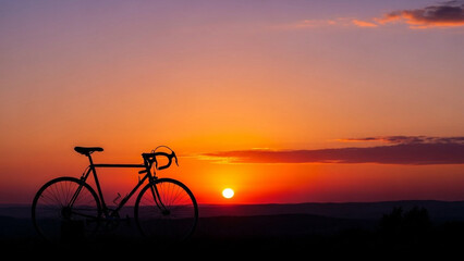 Obraz premium HSilhouette of a bicycle parked near a sunset horizon, warm sky gradient, peaceful outdoor atmosphere, no people visible.