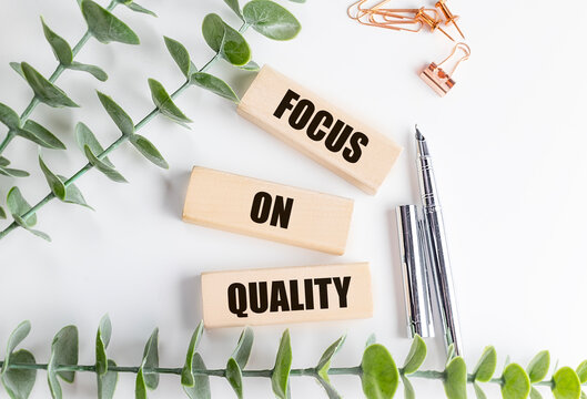 Focus on quality phrase on wooden blocks with office supplies, pen, and green plant on white background