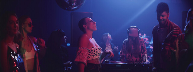 Exciting night at a club with lively dancing and a vibrant DJ performance in a colorful light setting