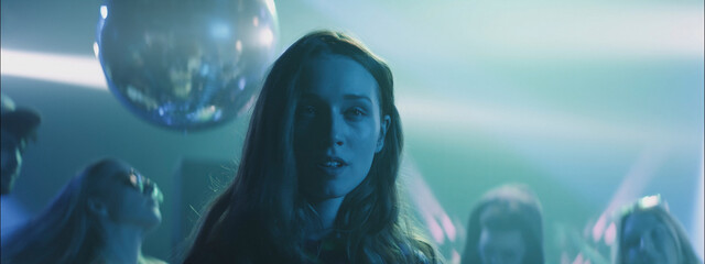 Young woman dancing at night club with colorful lights and a disco ball, creating a lively atmosphere with friends