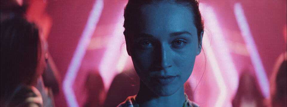 Evening party scene with vibrant lights and a young woman in focus at a lively venue - Powered by Adobe