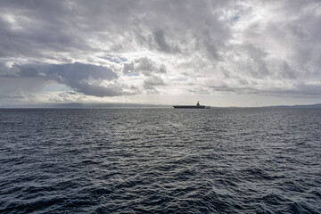 Massive Aircraft Carrier Silhouetted On Calm Sea Under Cloudy Sky For Military and Maritime Stock Use