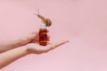 Glass cosmetic bottle with snail in hand. Mockup for your brand. Skin care product, spa, luxury,...