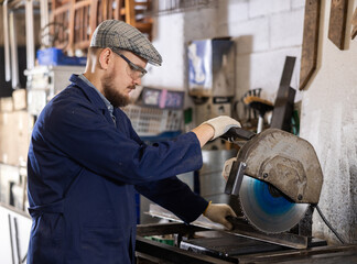Work in metalworking shop - man wearing safety glasses cuts a metal corner with a circular saw