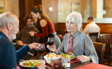 Happy elderly couple man and woman eating drinking and talking in restaurant
