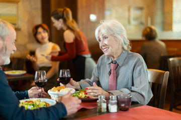 Happy elderly couple man and woman eating drinking and talking in restaurant