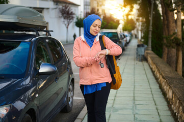 Muslim Woman In Hijab On City Street Checking Watch With Backpack And Car Nearby Today
