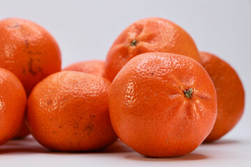 A Close Up Group Of Ripe Mandarin Oranges Piled On A White Surface. The Image Highlights The Vibrant Color And Porous Texture Of The Citrus Peel.
