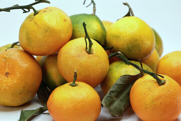 Close Up Of A Pile Of Ripe Mandarin Oranges With Textured Skin And Dry Leaves. A Natural Composition Of Citrus Fruits Isolated On A White Background.