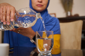 Woman In Hijab Pouring Water Into Glass At Home: Everyday Life Moment Of Hydration
