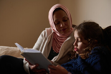 Mother And Daughter Reading Together At Home: Modern Muslim Woman In Hijab In Europe Lifestyle