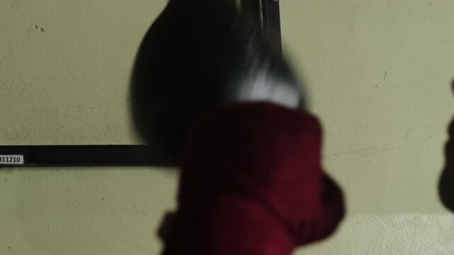 Athlete practices hitting speed bag practicing in dimly lit gym. Male boxer uses construction to increase hand speed skill and improve endurance
