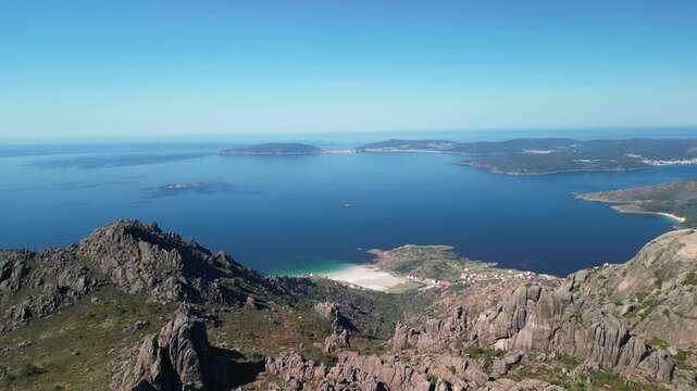 Aerial view of a stark contrast between the rugged, rocky mountains and the serene, deep blue sea with a white sandy beach, Carnota, A Coruna, Spain.