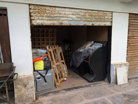 Garage entrance converted into storage room unit with junk, discarded appliances, furniture and rusted roller shutter. Clutter, disorganization, neglect, hoarding, renovation, urban decay, old.
