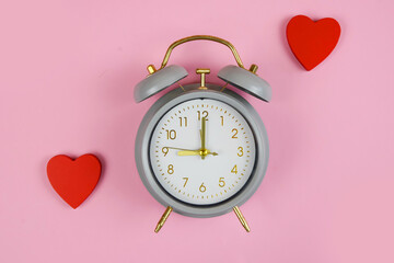 Vintage style alarm clock decorated with bright red hearts on a soft pink background for special occasions