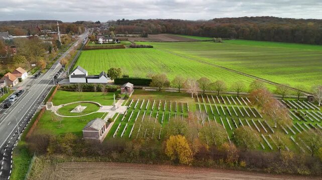 Aerial drone view of Hooge Crater Cemetery surrounded by open fields on former First World War battlefields, showing rows of graves and a peaceful landscape of remembrance.
