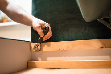 Man disassembling sofa furniture mechanism at home using furniture wrench. DIY Assembling Furniture concept.