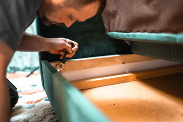 Man disassembling sofa furniture mechanism at home using furniture wrench. DIY Assembling Furniture concept.