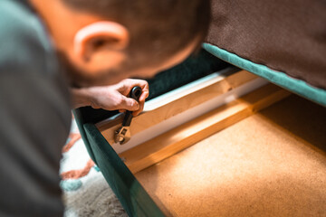Man disassembling sofa furniture mechanism at home using furniture wrench. DIY Assembling Furniture concept.