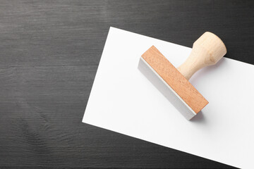 One wooden stamp and blank sheet of paper on black table, top view. Space for text