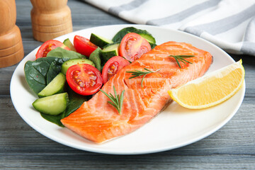 Piece of tasty grilled salmon, lemon, rosemary and salad on grey wooden table, closeup