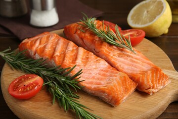 Pieces of tasty grilled salmon, rosemary and tomatoes on wooden table, closeup